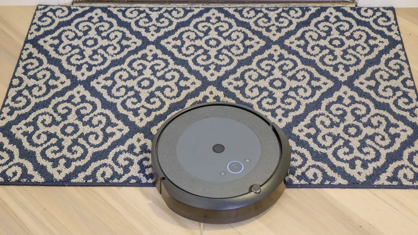 Robotdammsugare på väg upp på en blåmönstrad matta på ett ljust trägolv